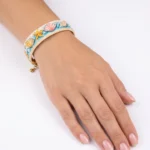 دستبند میوکی طرح صدف دریایی پوشیده‌شده روی مچ دست با قفل و آویز طلایی، پس‌زمینه سفید
