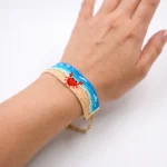 دستبند میوکی طرح ساحل و خرچنگ پوشیده‌شده روی مچ دست با زنجیر تنظیم طلایی آویزان، پس‌زمینه سفید