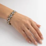 دستبند میوکی مشکی طلایی طرح موزاییکی پوشیده‌شده روی مچ دست، پس‌زمینه سفید