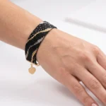 دستبند میوکی مشکی پهن بسته شده روی مچ دست با آویز قلب طلایی