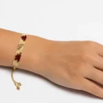 دستبند بافت میوکی با طرح ستاره قرمز روی زمینه کرم و بژ، بسته‌شده روی مچ دست با بند طلایی قابل تنظیم