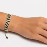 دستبند بافت میوکی طرح شورون مشکی و طلایی بسته‌شده روی مچ دست با بند نخی طلایی