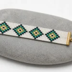 دستبند بافت میوکی طرح لوزی طلایی و سبز قرارگرفته روی سنگ خاکستری با بست فلزی طلایی