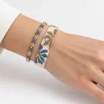 ست دستبند بافت میوکی پهن طرح گل و دستبند باریک مهره‌ای بسته‌شده روی مچ دست به‌صورت هم‌زمان