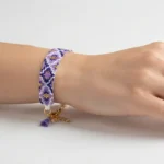 دستبند میوکی بنفش با طرح لوزی و منگوله آویز، بسته شده روی مچ دست